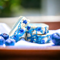 Soap bar that is  cream with blue swirls. The soap bar is topped with small blueberry  soap 