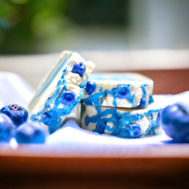 Soap bar that is  cream with blue swirls. The soap bar is topped with small blueberry  soap 
